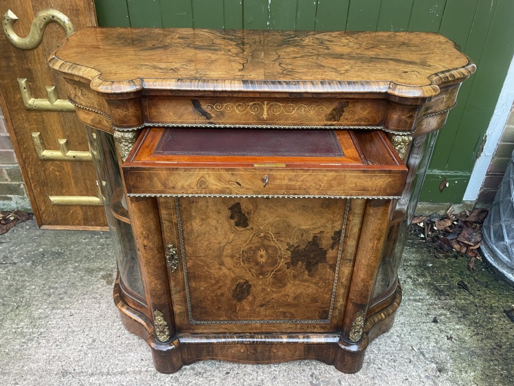 A mid-19th century Victorian burr walnut credenza featuring boxwood marquetry inlay, gilded ormolu mounts, a central drawer, and curved glass side display doors. View II