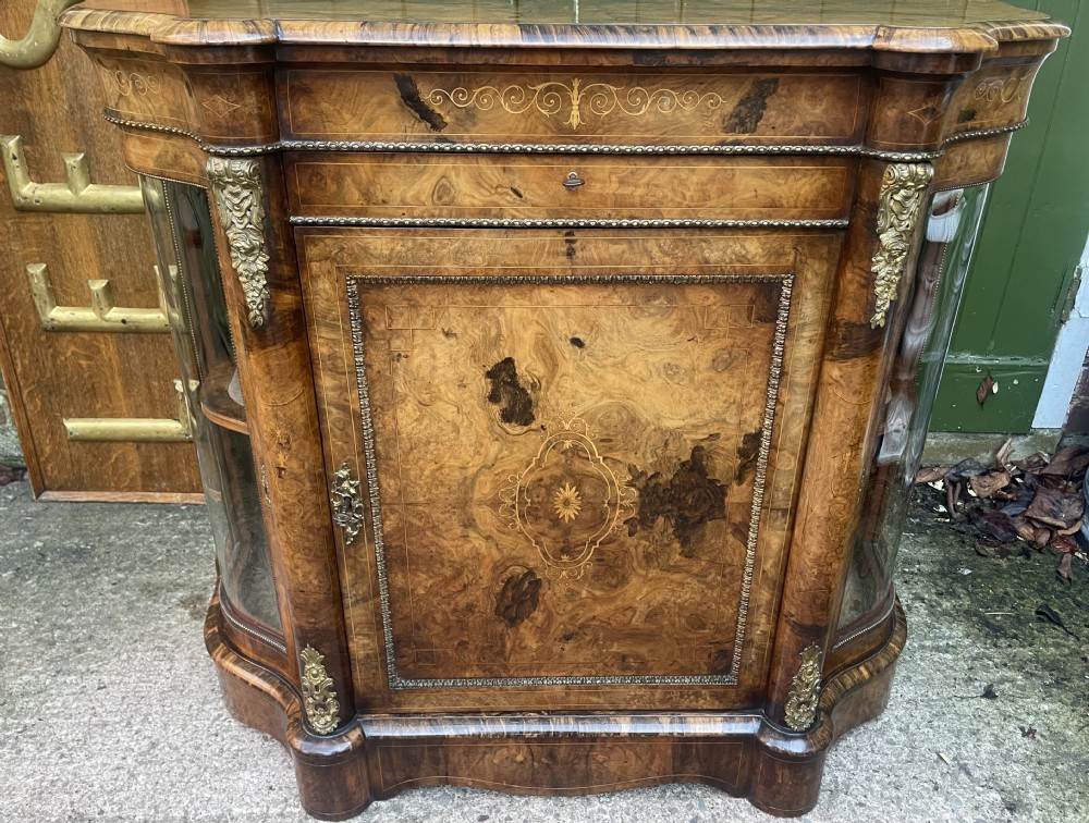 A mid-19th century Victorian burr walnut credenza featuring boxwood marquetry inlay, gilded ormolu mounts, a central drawer, and curved glass side display doors. View XXIV