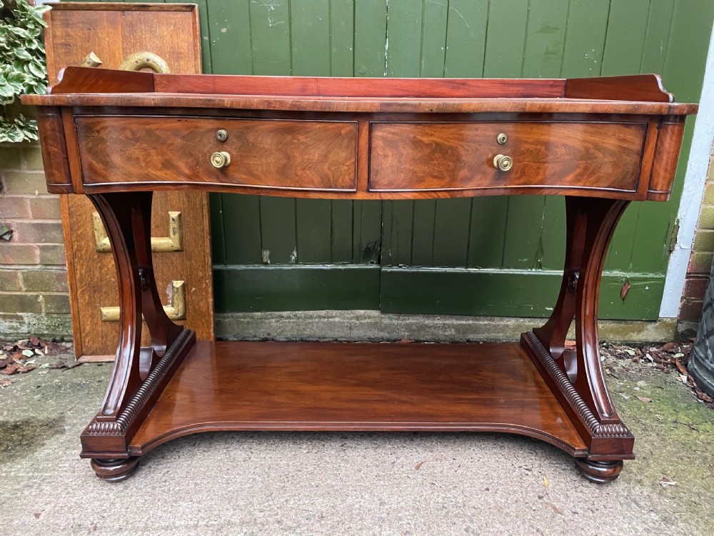 An early nineteenth-century mahogany serpentine side table featuring two drawers, a gallery top, curved end supports, and a lower shelf. View II