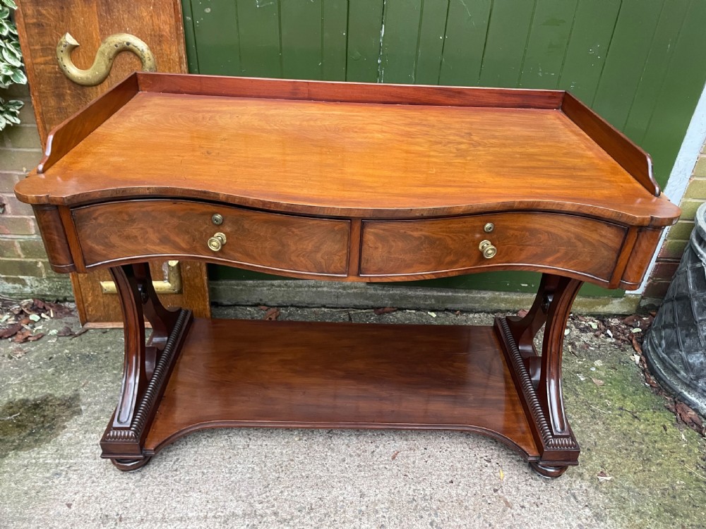 An early nineteenth-century mahogany serpentine side table featuring two drawers, a gallery top, curved end supports, and a lower shelf. View III