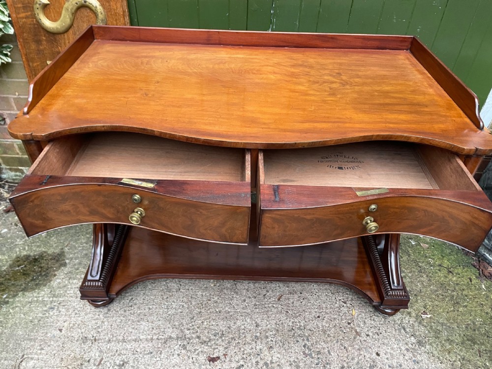 An early nineteenth-century mahogany serpentine side table featuring two drawers, a gallery top, curved end supports, and a lower shelf. View VI