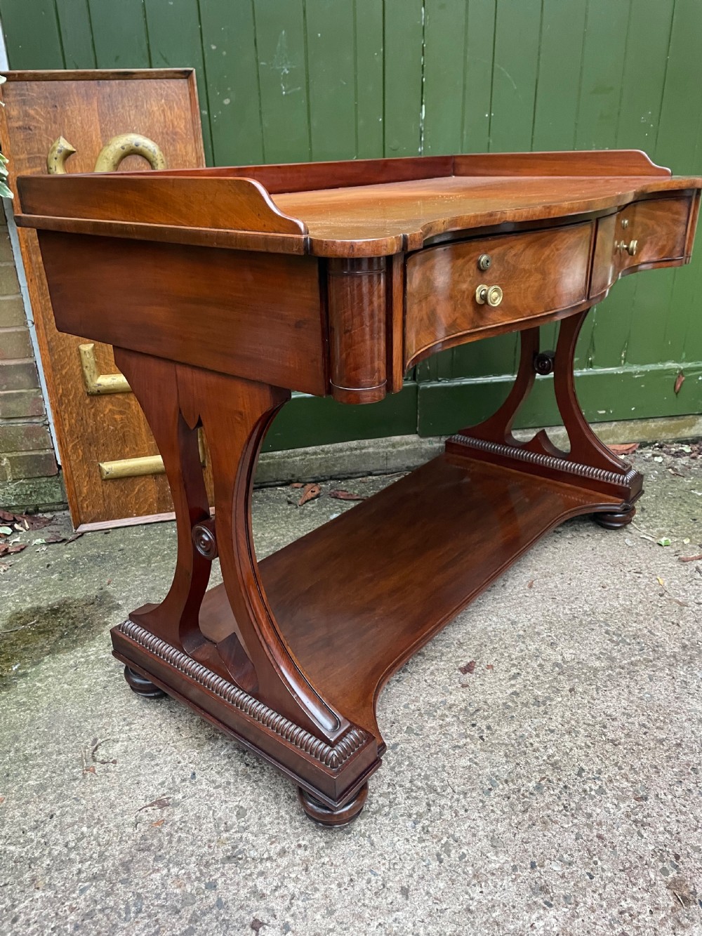 An early nineteenth-century mahogany serpentine side table featuring two drawers, a gallery top, curved end supports, and a lower shelf. View VIII