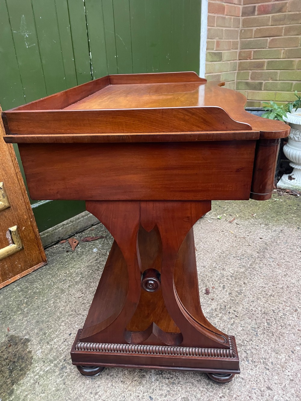 An early nineteenth-century mahogany serpentine side table featuring two drawers, a gallery top, curved end supports, and a lower shelf. View X