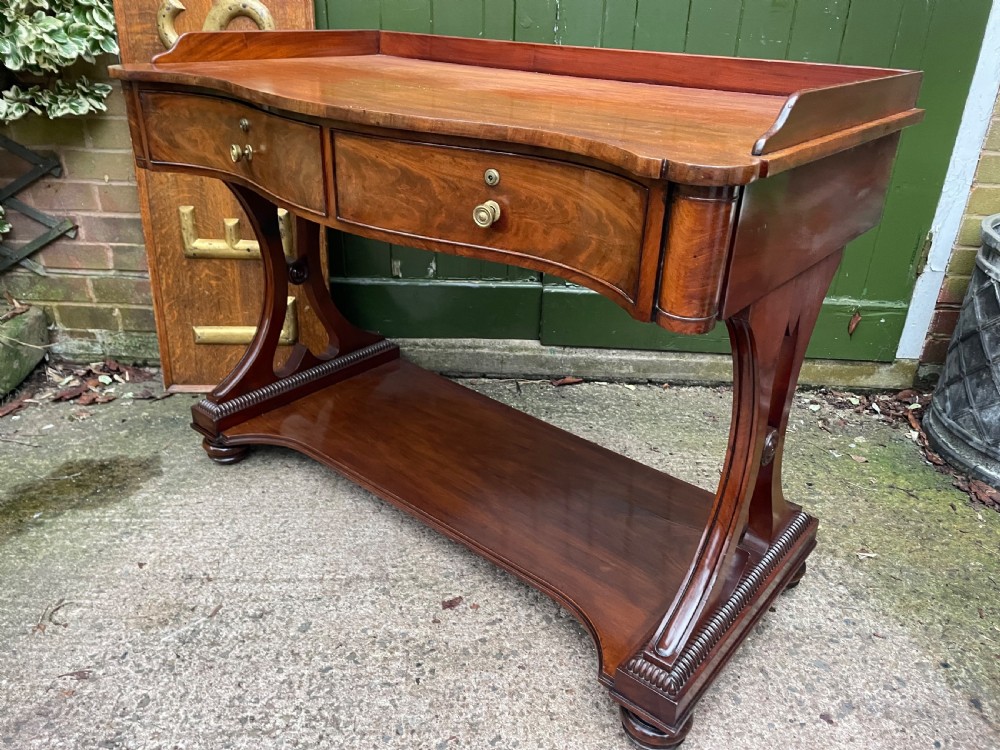 An early nineteenth-century mahogany serpentine side table featuring two drawers, a gallery top, curved end supports, and a lower shelf. View XI