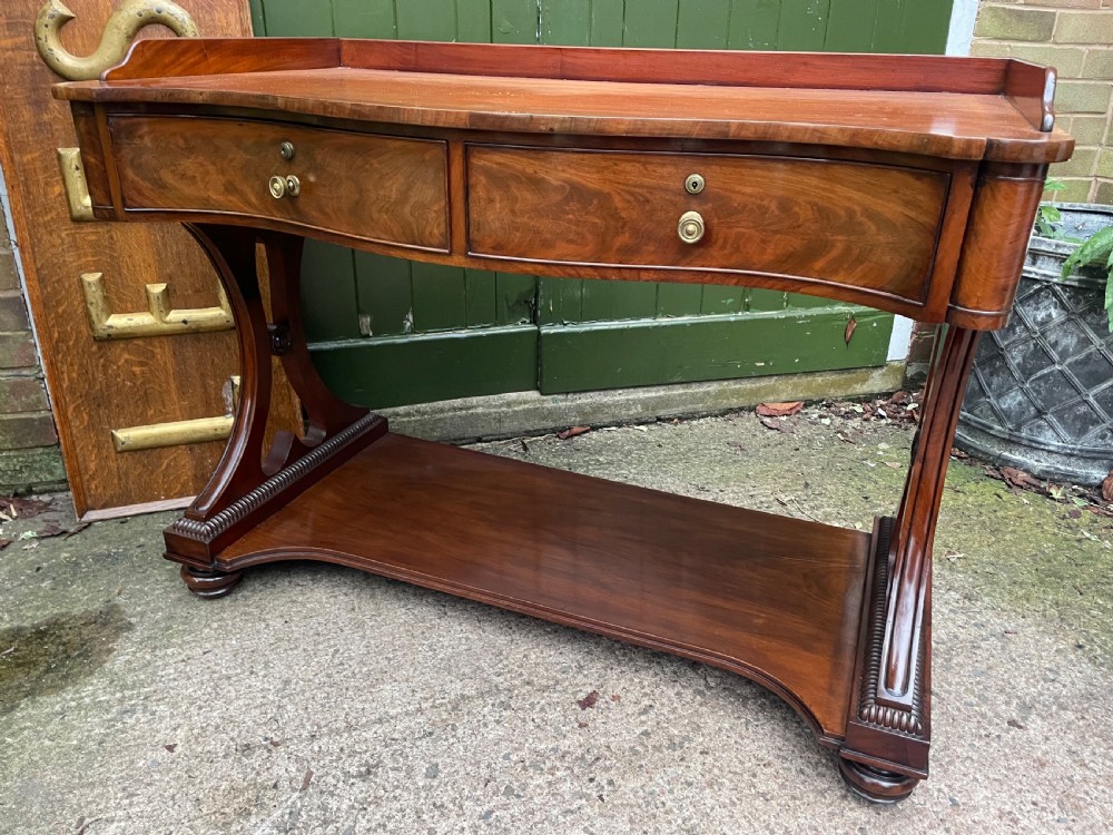An early nineteenth-century mahogany serpentine side table featuring two drawers, a gallery top, curved end supports, and a lower shelf. View XV