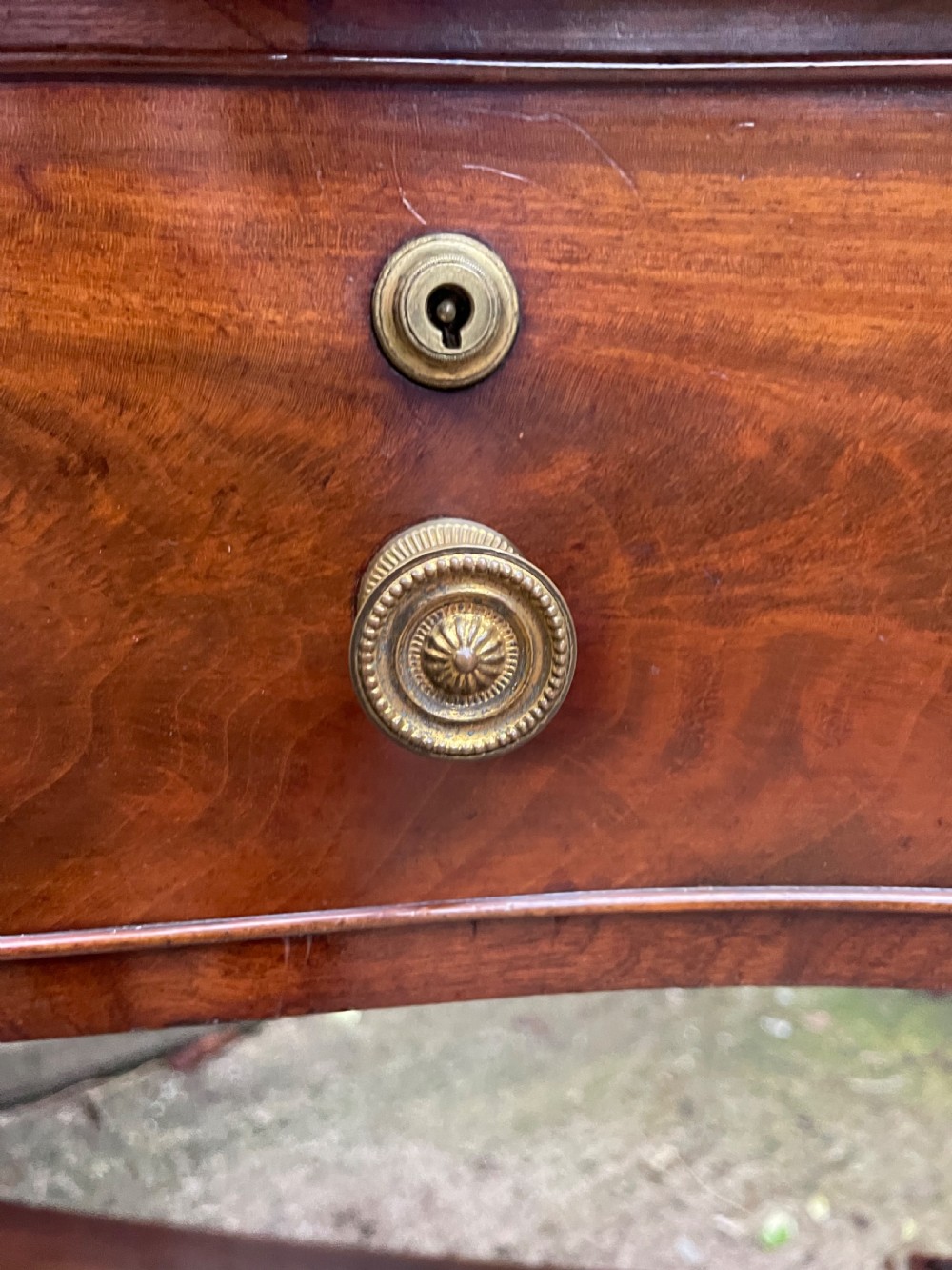 An early nineteenth-century mahogany serpentine side table featuring two drawers, a gallery top, curved end supports, and a lower shelf. View XVI