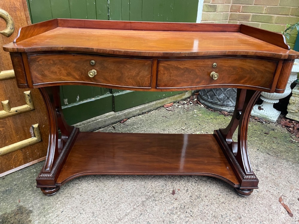 An early nineteenth-century mahogany serpentine side table featuring two drawers, a gallery top, curved end supports, and a lower shelf. View XIX