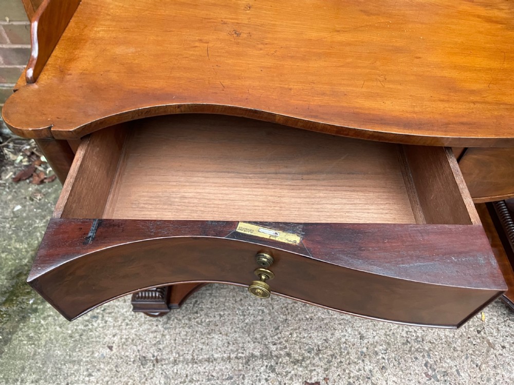 An early nineteenth-century mahogany serpentine side table featuring two drawers, a gallery top, curved end supports, and a lower shelf. View VII