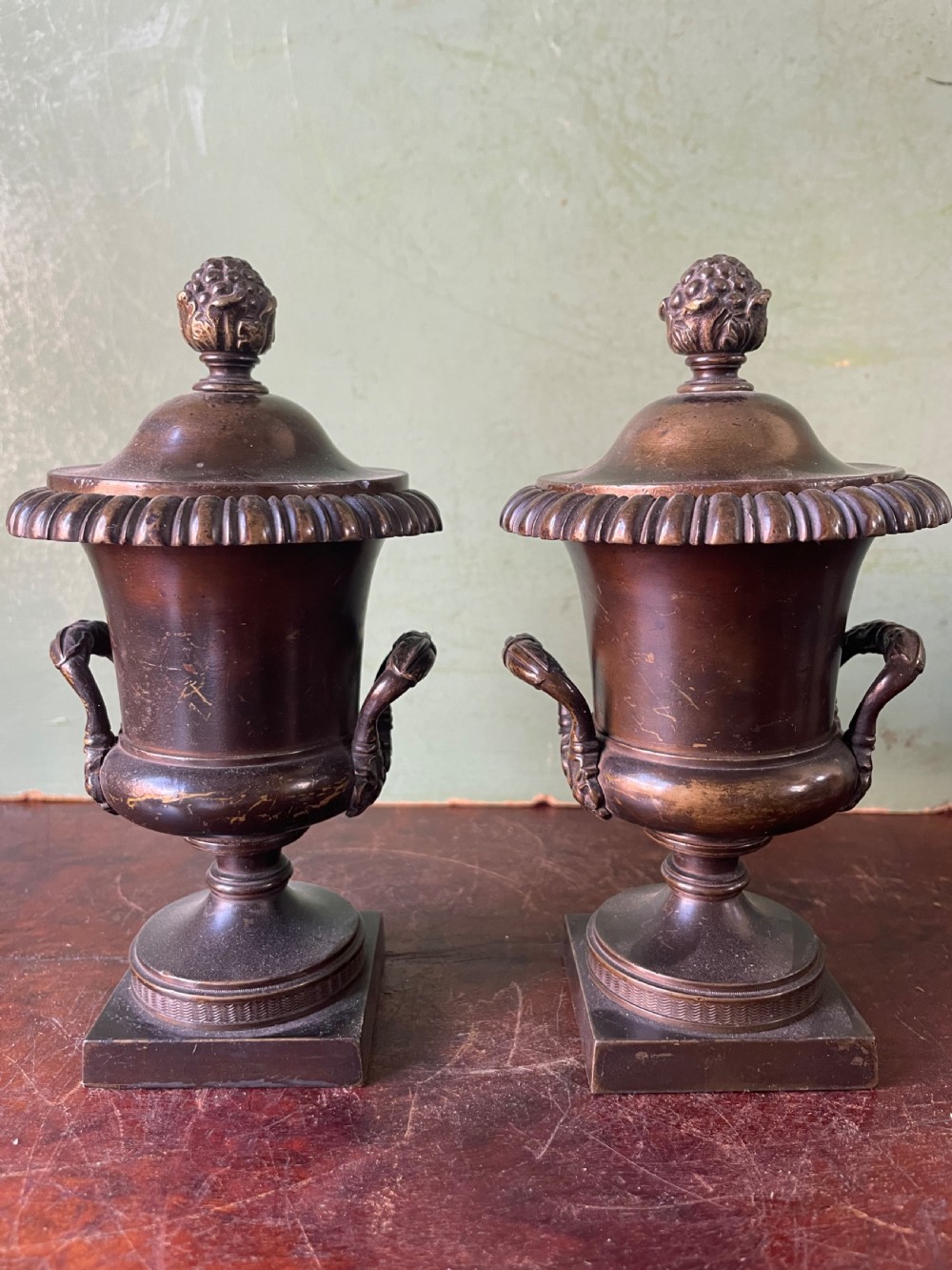 A pair of early nineteenth-century Regency dark brown bronze cassolettes with campana-shaped bodies, double loop handles, gadrooned lids topped with finials, resting on square plinth bases.