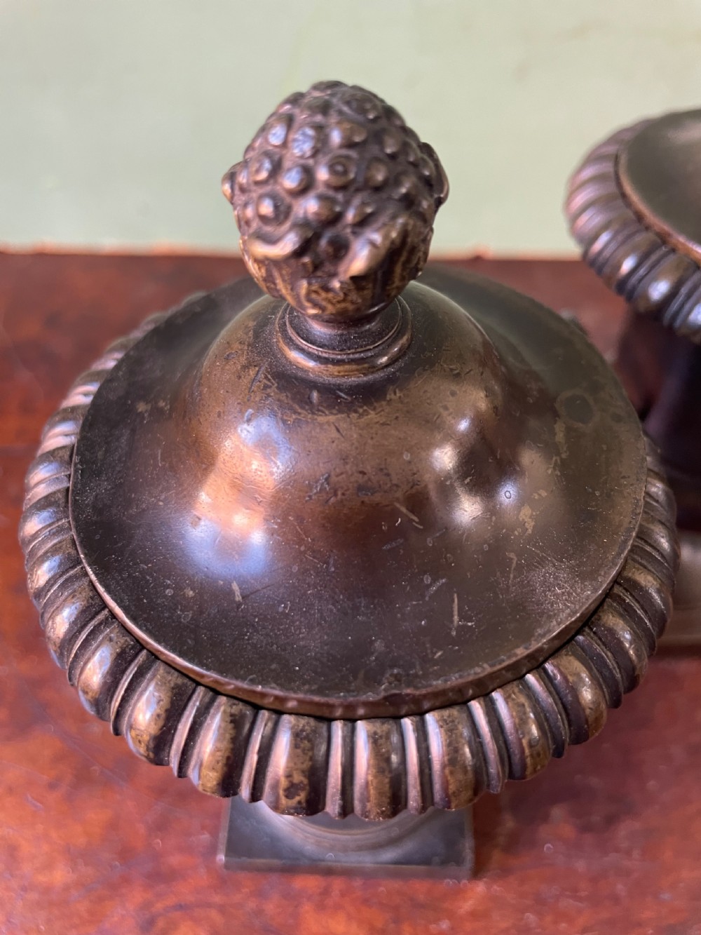 A pair of early nineteenth-century Regency dark brown bronze cassolettes with campana-shaped bodies, double loop handles, gadrooned lids topped with finials, resting on square plinth bases. View XIV
