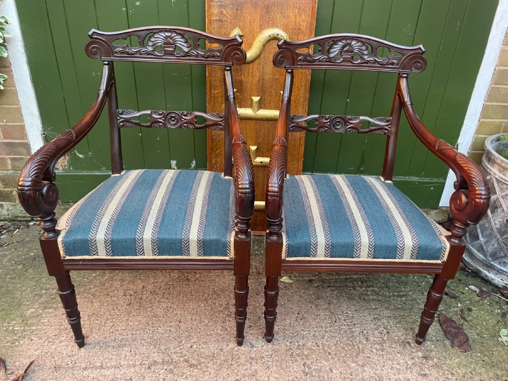 A pair of early 19th-century carved mahogany salon armchairs featuring carved crest rails, scrolled armrests, turned front legs, and blue striped fabric upholstery. View II