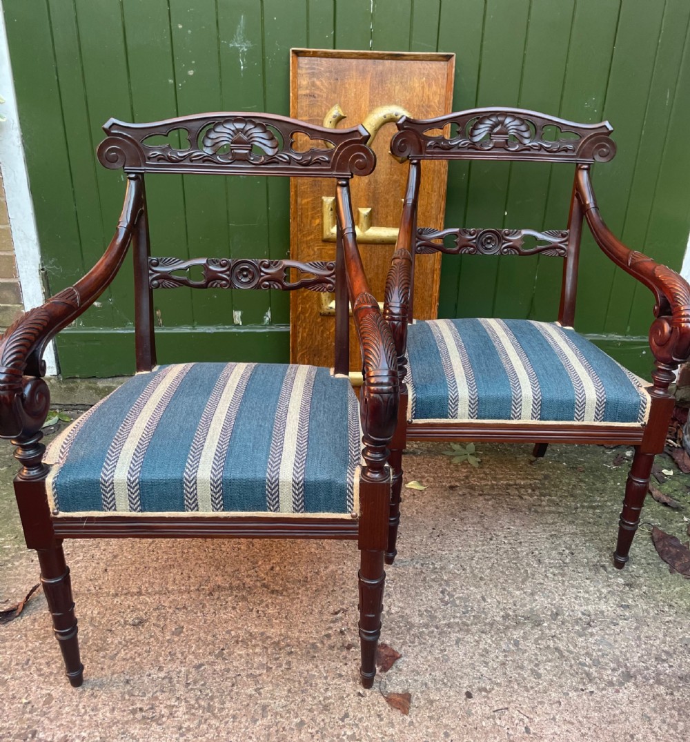 A pair of early 19th-century carved mahogany salon armchairs featuring carved crest rails, scrolled armrests, turned front legs, and blue striped fabric upholstery. View III