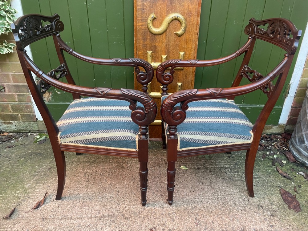 A pair of early 19th-century carved mahogany salon armchairs featuring carved crest rails, scrolled armrests, turned front legs, and blue striped fabric upholstery. View V