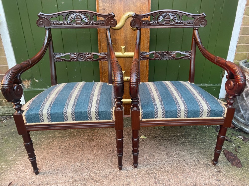 A pair of early 19th-century carved mahogany salon armchairs featuring carved crest rails, scrolled armrests, turned front legs, and blue striped fabric upholstery. View VI