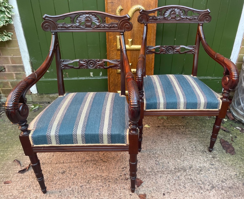 A pair of early 19th-century carved mahogany salon armchairs featuring carved crest rails, scrolled armrests, turned front legs, and blue striped fabric upholstery. View VII