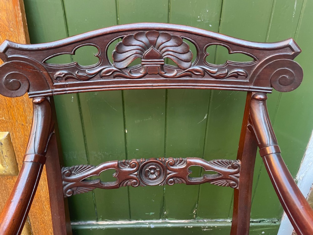 A pair of early 19th-century carved mahogany salon armchairs featuring carved crest rails, scrolled armrests, turned front legs, and blue striped fabric upholstery. View X