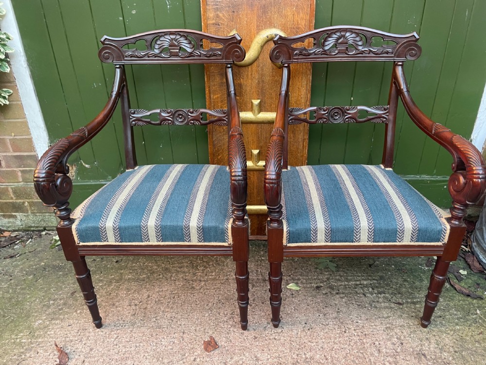 A pair of early 19th-century carved mahogany salon armchairs featuring carved crest rails, scrolled armrests, turned front legs, and blue striped fabric upholstery. View XIV