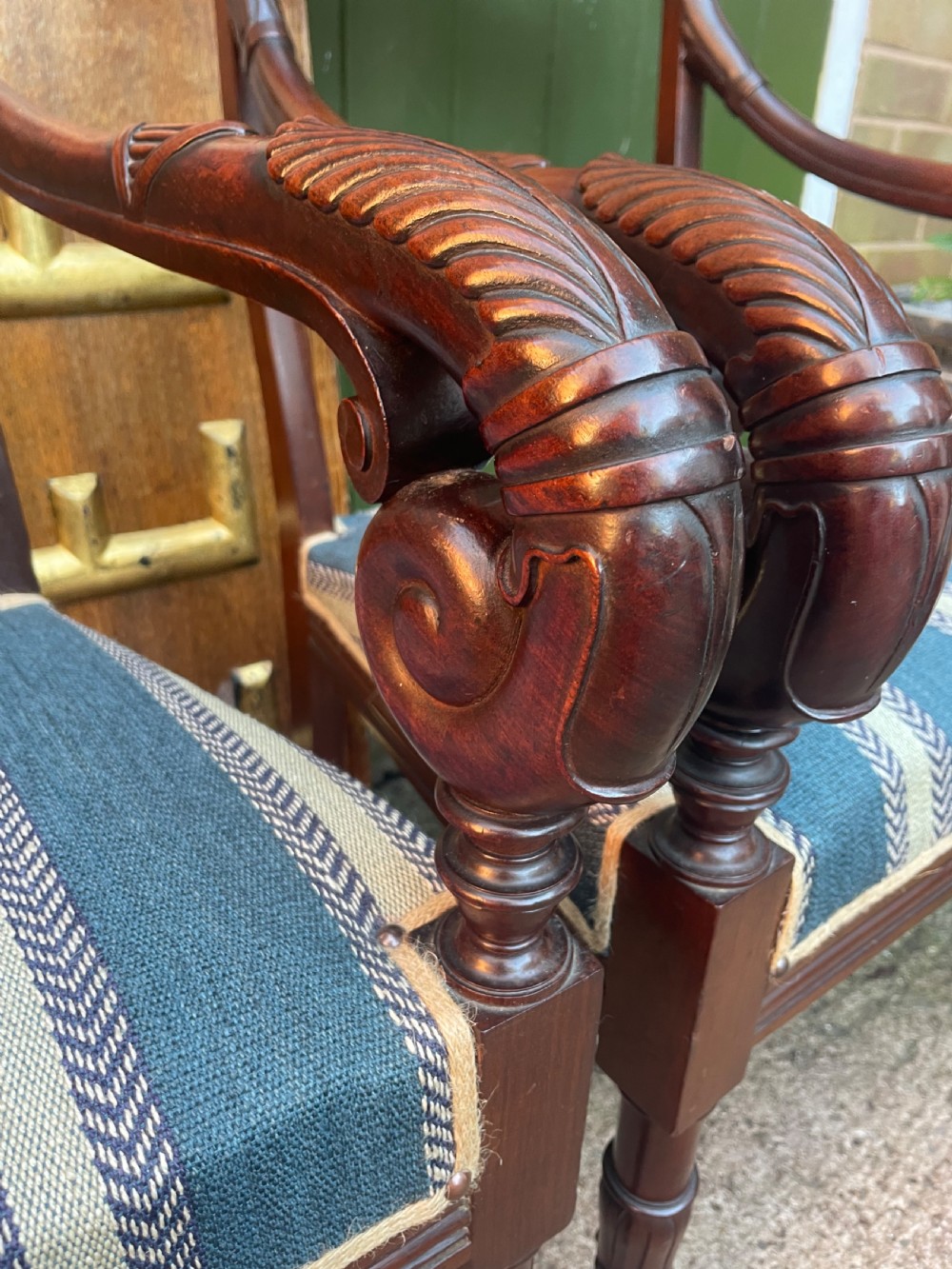 A pair of early 19th-century carved mahogany salon armchairs featuring carved crest rails, scrolled armrests, turned front legs, and blue striped fabric upholstery. View XVI