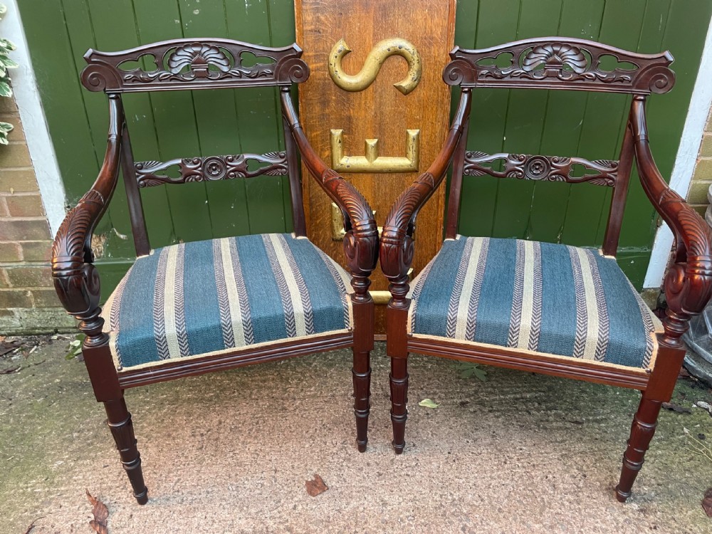 A pair of early 19th-century carved mahogany salon armchairs featuring carved crest rails, scrolled armrests, turned front legs, and blue striped fabric upholstery. View XVII