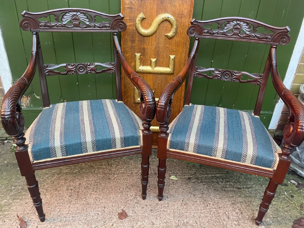 A pair of early 19th-century carved mahogany salon armchairs featuring carved crest rails, scrolled armrests, turned front legs, and blue striped fabric upholstery. View XVIII