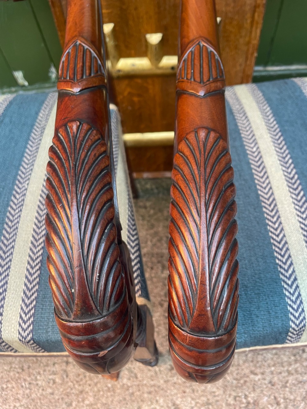 A pair of early 19th-century carved mahogany salon armchairs featuring carved crest rails, scrolled armrests, turned front legs, and blue striped fabric upholstery. View XXIV