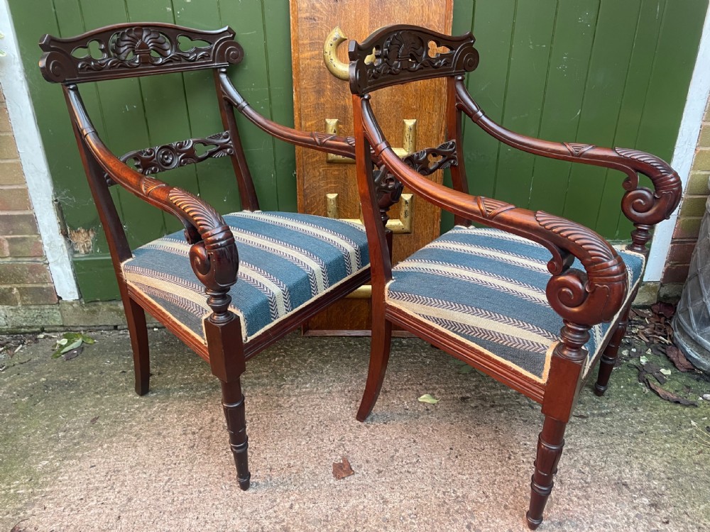 A pair of early 19th-century carved mahogany salon armchairs featuring carved crest rails, scrolled armrests, turned front legs, and blue striped fabric upholstery. View XXV