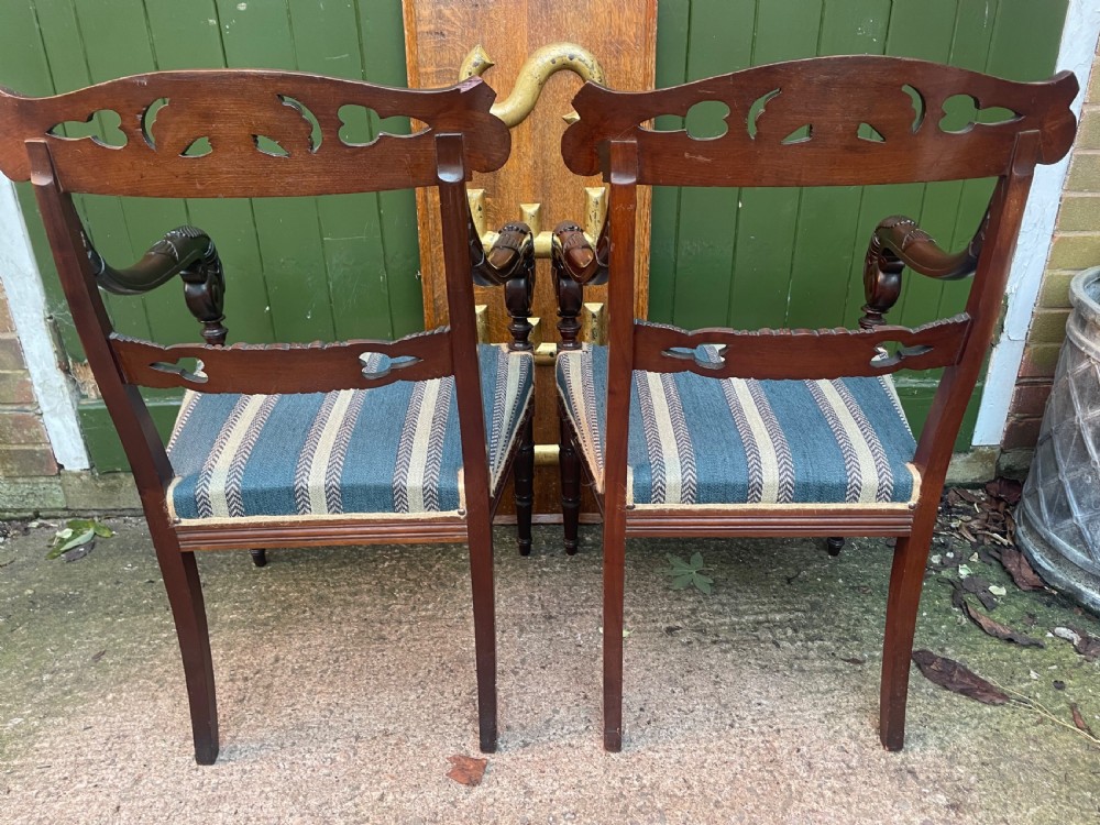 A pair of early 19th-century carved mahogany salon armchairs featuring carved crest rails, scrolled armrests, turned front legs, and blue striped fabric upholstery. View XXVII