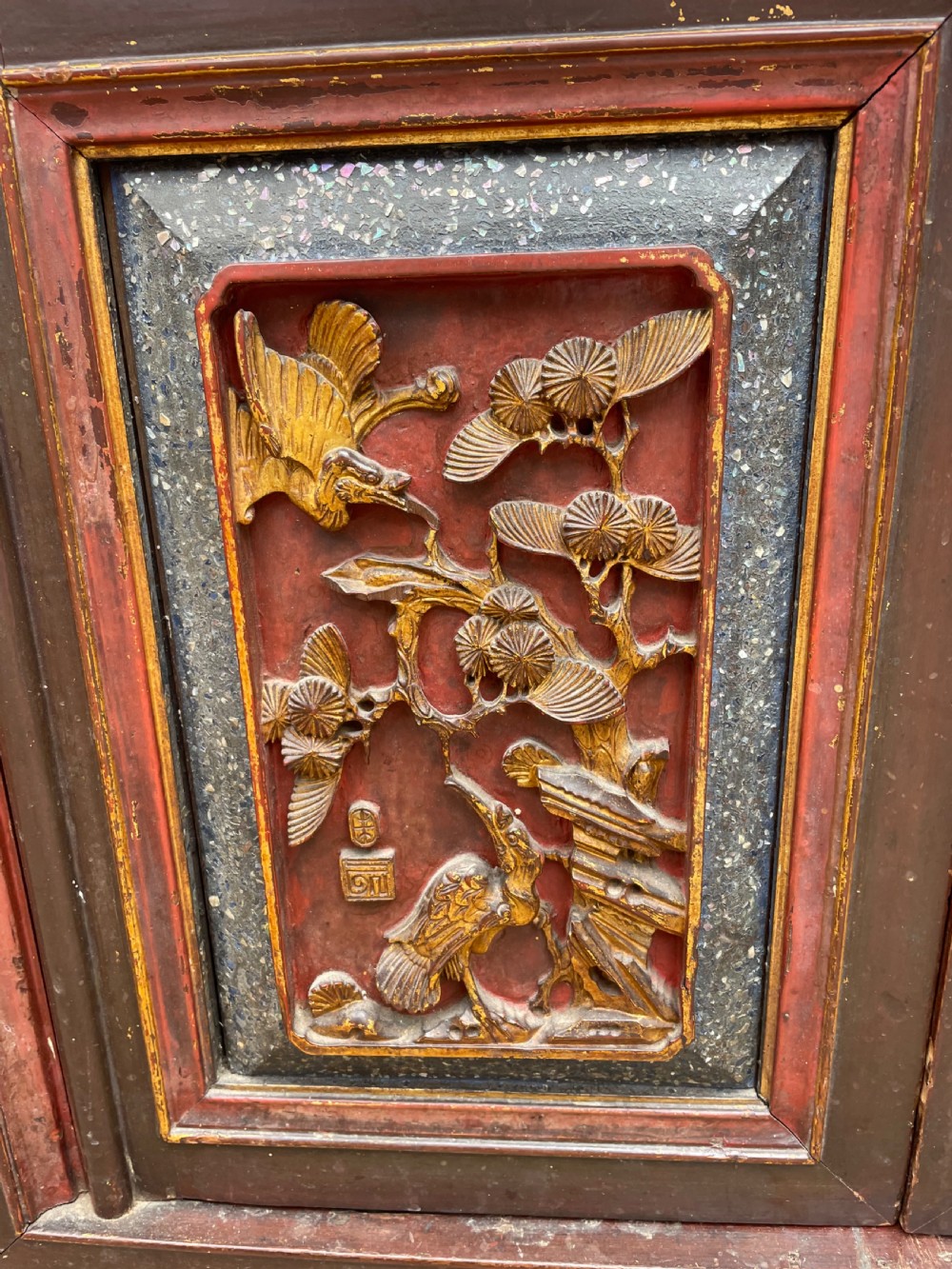 A late nineteenth-century Chinese Qing Dynasty red lacquered side cabinet featuring relief-carved gilded wood panels depicted with architectural scenes, figures, and foliage. View VII
