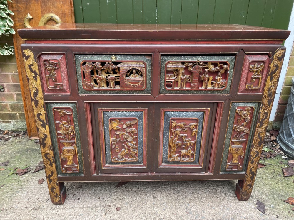 A late nineteenth-century Chinese Qing Dynasty red lacquered side cabinet featuring relief-carved gilded wood panels depicted with architectural scenes, figures, and foliage. View XIII
