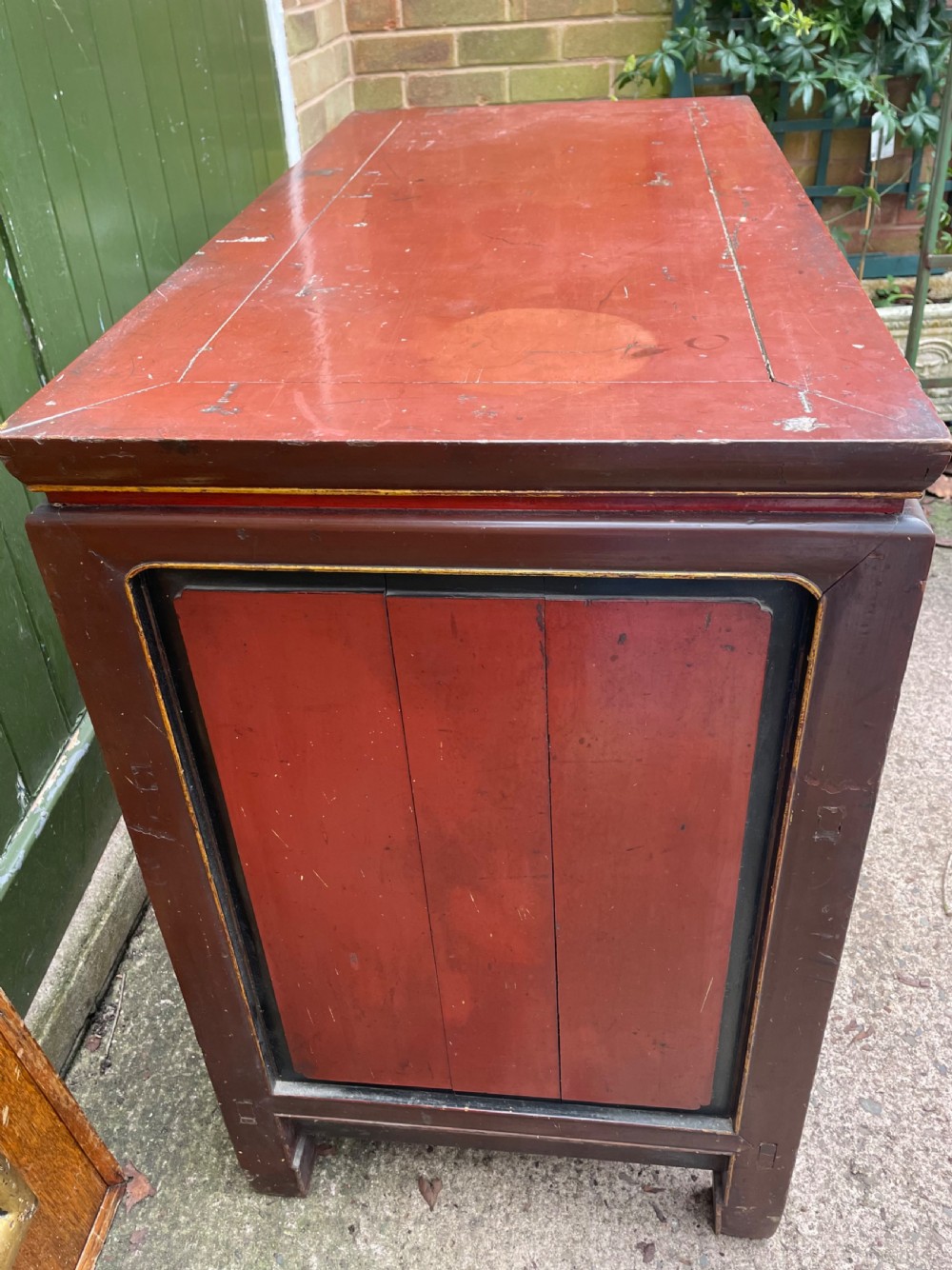 A late nineteenth-century Chinese Qing Dynasty red lacquered side cabinet featuring relief-carved gilded wood panels depicted with architectural scenes, figures, and foliage. View XV