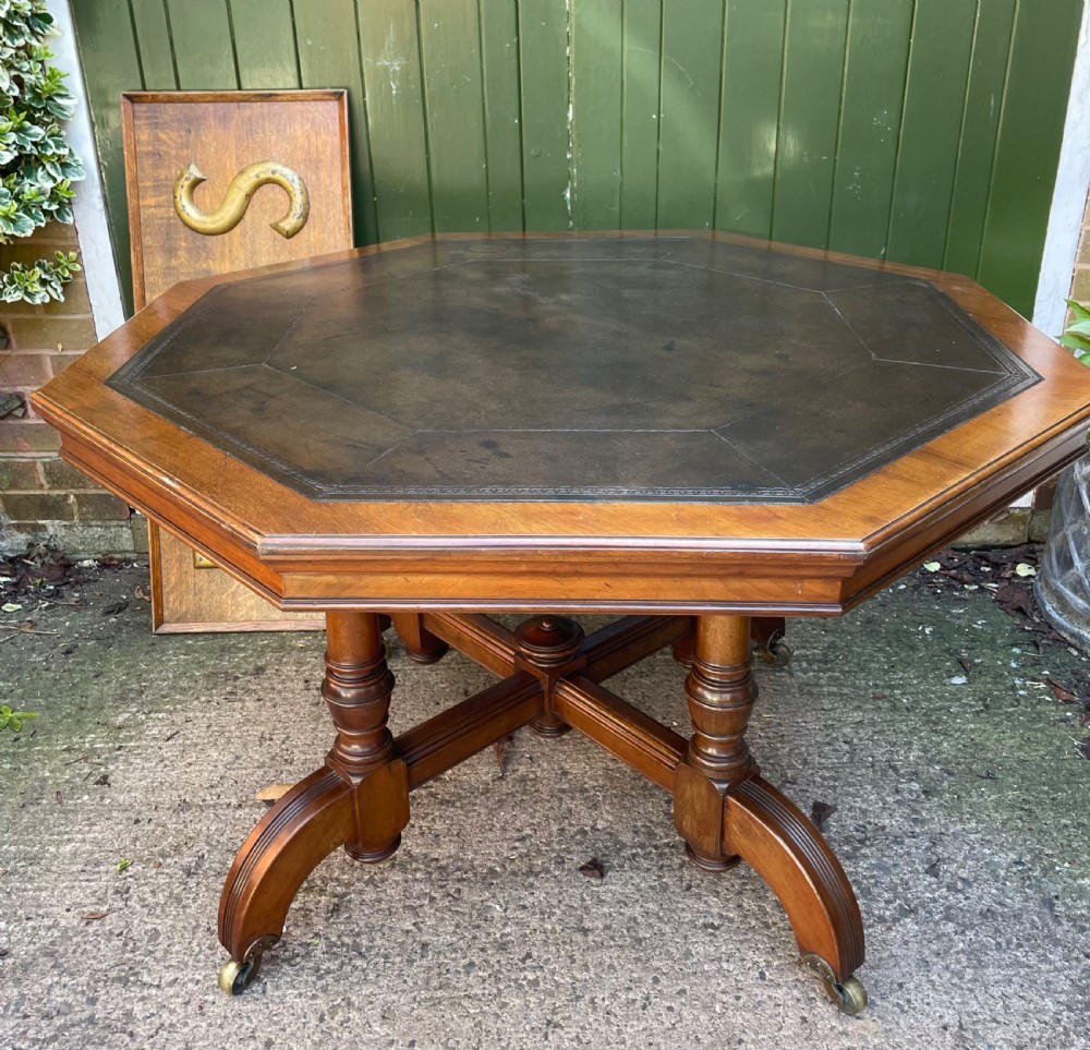 A late nineteenth-century octagonal walnut library table featuring a tooled dark leather inset top, turned legs, a cross stretcher, and brass castors.