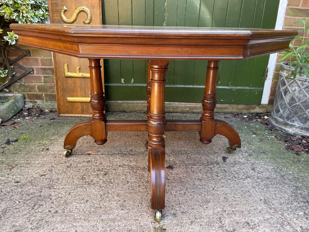 A late nineteenth-century octagonal walnut library table featuring a tooled dark leather inset top, turned legs, a cross stretcher, and brass castors. View XIX