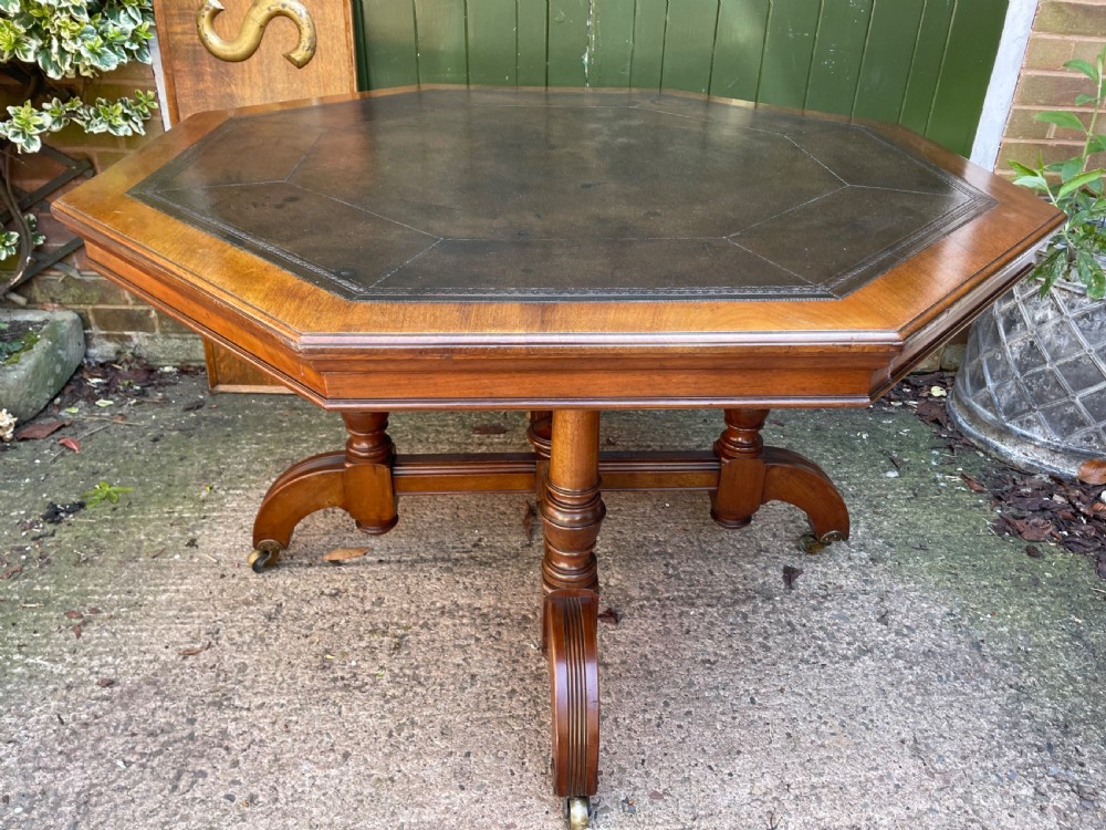 A late nineteenth-century octagonal walnut library table featuring a tooled dark leather inset top, turned legs, a cross stretcher, and brass castors. View XXI