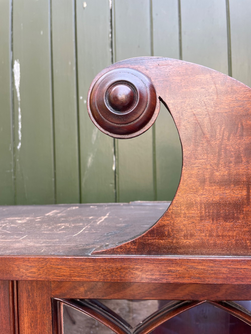 An early nineteenth-century Regency mahogany glazed bookcase cabinet featuring a scroll pediment, Gothic arch astragal glazing, flame mahogany lower cupboard panels, and turned side columns. View VI