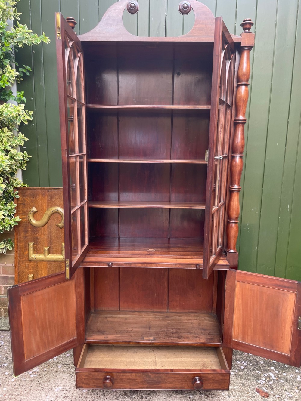 An early nineteenth-century Regency mahogany glazed bookcase cabinet featuring a scroll pediment, Gothic arch astragal glazing, flame mahogany lower cupboard panels, and turned side columns. View IX