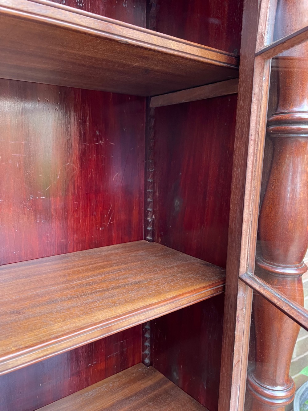 An early nineteenth-century Regency mahogany glazed bookcase cabinet featuring a scroll pediment, Gothic arch astragal glazing, flame mahogany lower cupboard panels, and turned side columns. View X