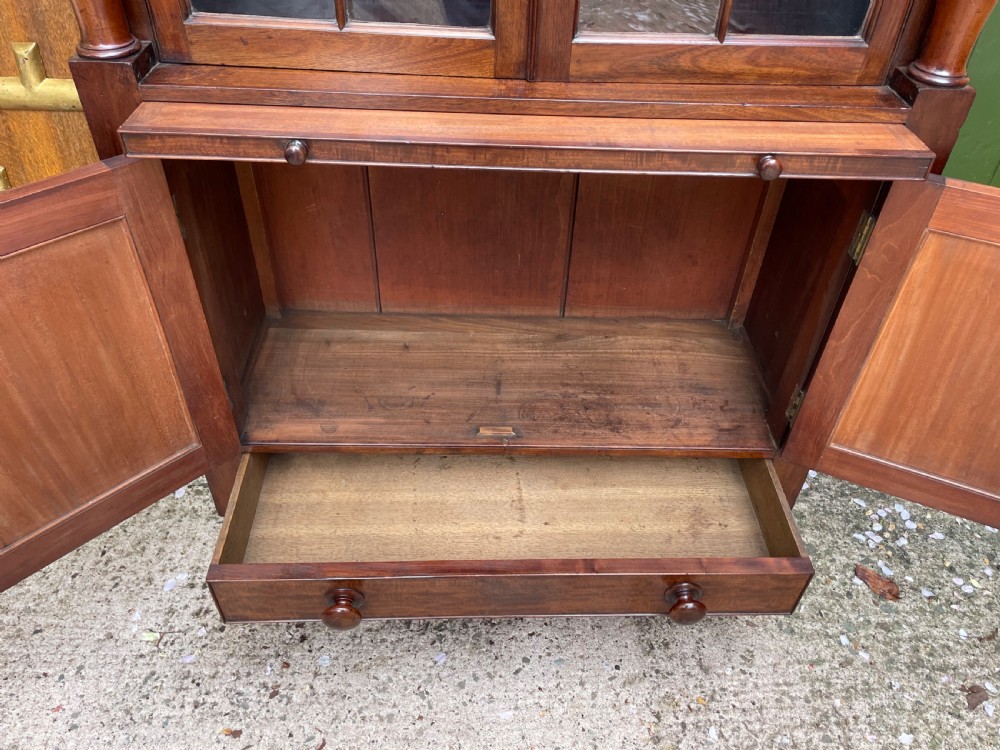 An early nineteenth-century Regency mahogany glazed bookcase cabinet featuring a scroll pediment, Gothic arch astragal glazing, flame mahogany lower cupboard panels, and turned side columns. View XII