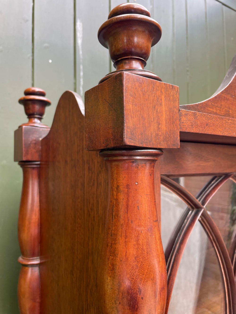 An early nineteenth-century Regency mahogany glazed bookcase cabinet featuring a scroll pediment, Gothic arch astragal glazing, flame mahogany lower cupboard panels, and turned side columns. View XV