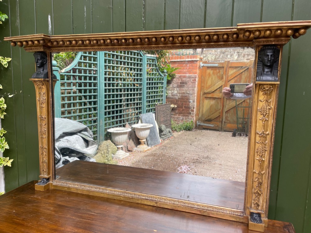 An early nineteenth-century Regency giltwood overmantel mirror featuring ball moulding along the cornice and ebonised Egyptian sphinx heads atop decorative pilasters. View II