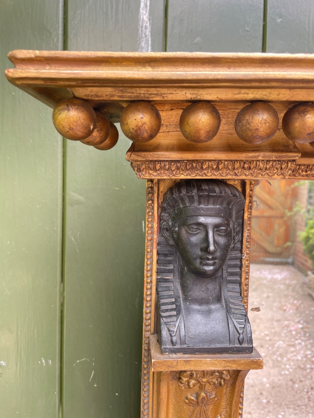 An early nineteenth-century Regency giltwood overmantel mirror featuring ball moulding along the cornice and ebonised Egyptian sphinx heads atop decorative pilasters. View III