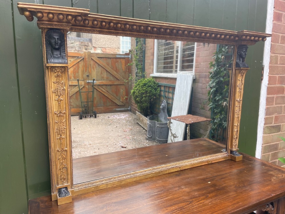An early nineteenth-century Regency giltwood overmantel mirror featuring ball moulding along the cornice and ebonised Egyptian sphinx heads atop decorative pilasters. View V