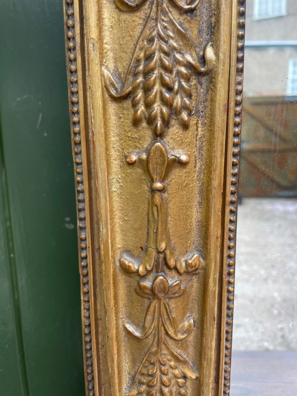 An early nineteenth-century Regency giltwood overmantel mirror featuring ball moulding along the cornice and ebonised Egyptian sphinx heads atop decorative pilasters. View VII