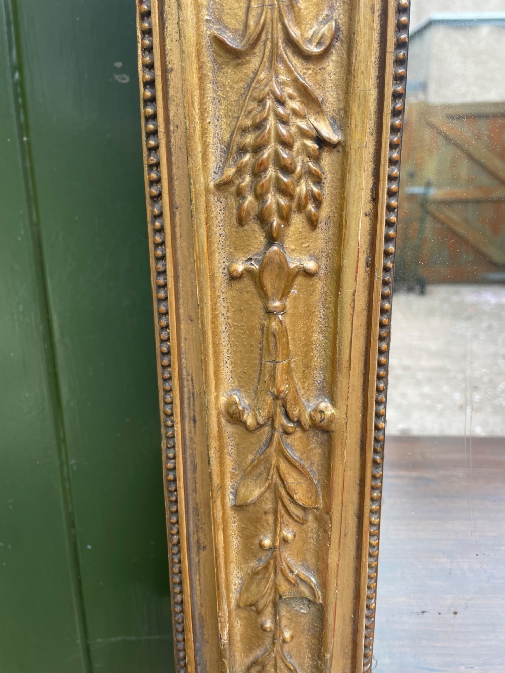 An early nineteenth-century Regency giltwood overmantel mirror featuring ball moulding along the cornice and ebonised Egyptian sphinx heads atop decorative pilasters. View VIII