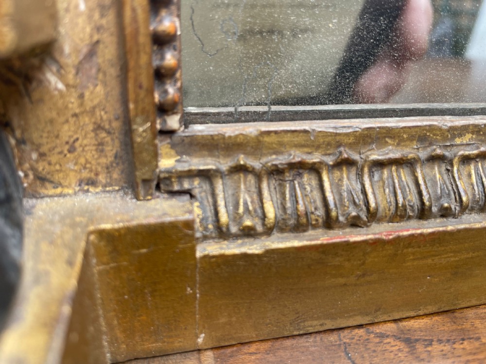 An early nineteenth-century Regency giltwood overmantel mirror featuring ball moulding along the cornice and ebonised Egyptian sphinx heads atop decorative pilasters. View X