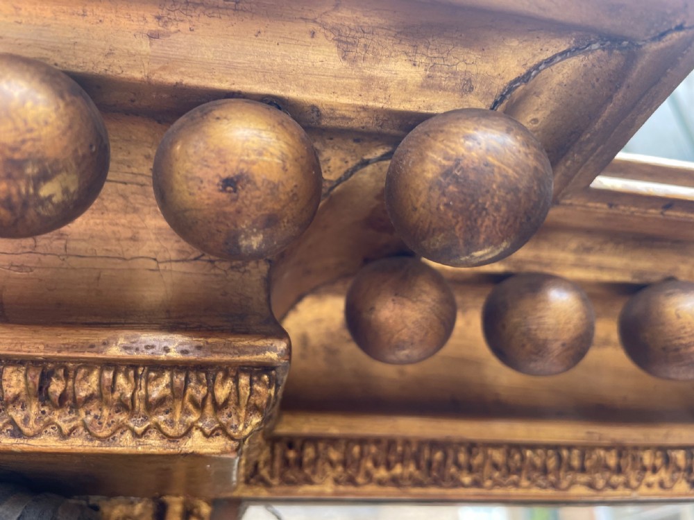 An early nineteenth-century Regency giltwood overmantel mirror featuring ball moulding along the cornice and ebonised Egyptian sphinx heads atop decorative pilasters. View XI