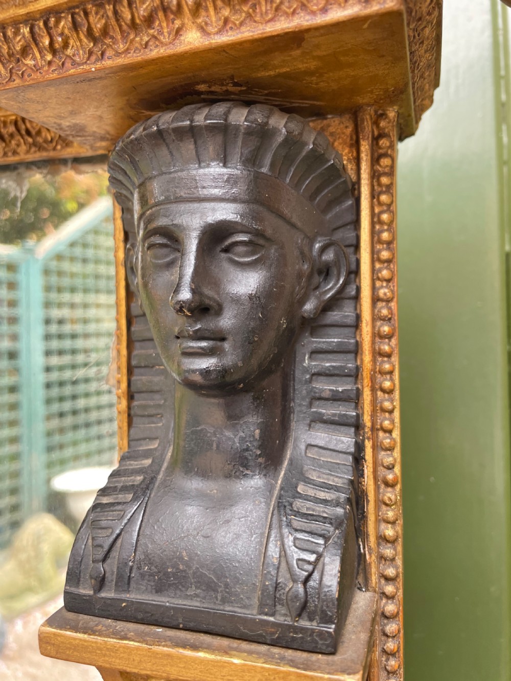 An early nineteenth-century Regency giltwood overmantel mirror featuring ball moulding along the cornice and ebonised Egyptian sphinx heads atop decorative pilasters. View XIII