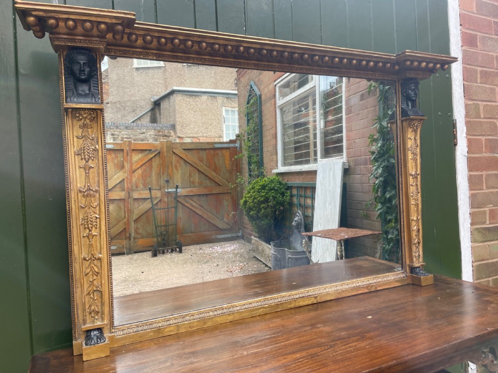 An early nineteenth-century Regency giltwood overmantel mirror featuring ball moulding along the cornice and ebonised Egyptian sphinx heads atop decorative pilasters. View XV