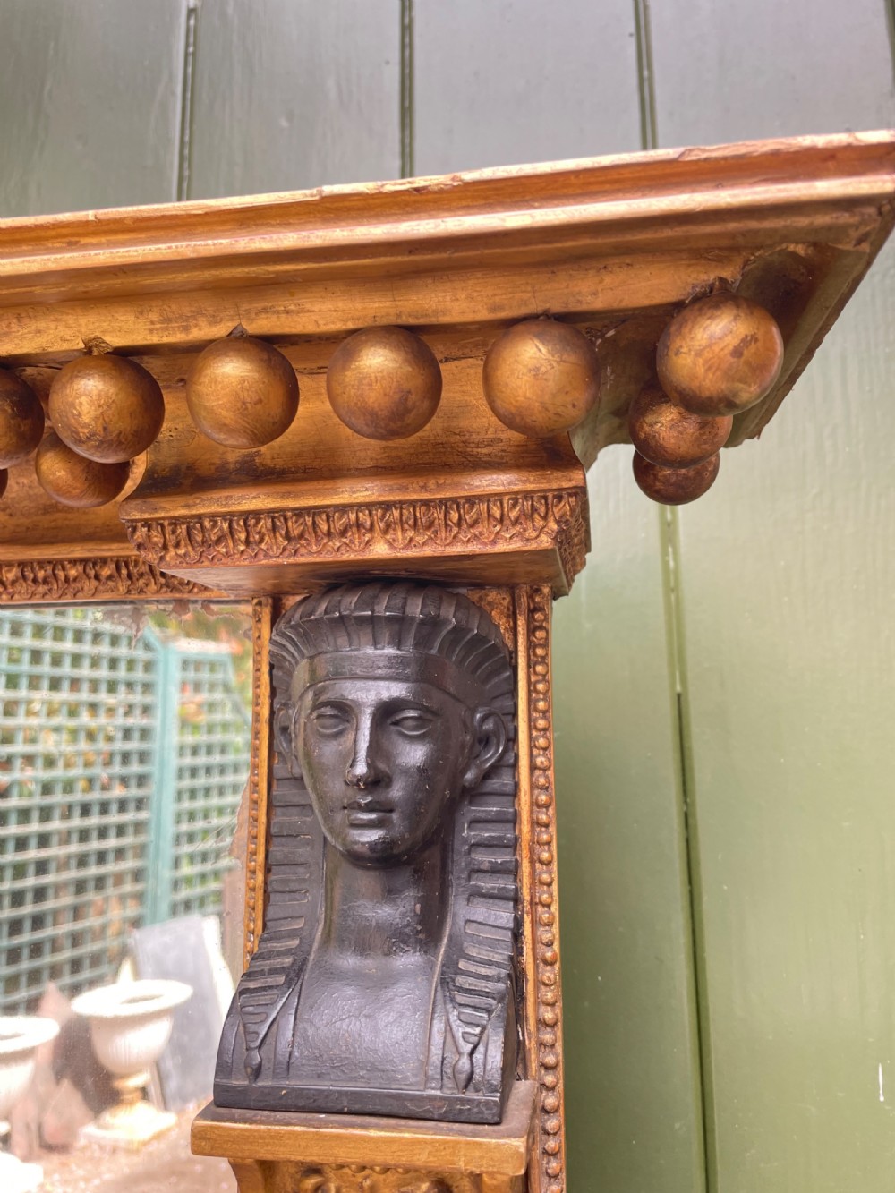 An early nineteenth-century Regency giltwood overmantel mirror featuring ball moulding along the cornice and ebonised Egyptian sphinx heads atop decorative pilasters. View XVIII