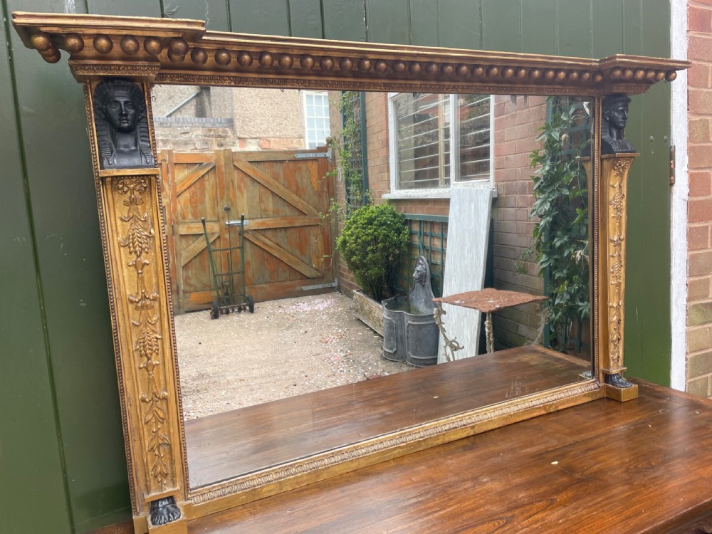 An early nineteenth-century Regency giltwood overmantel mirror featuring ball moulding along the cornice and ebonised Egyptian sphinx heads atop decorative pilasters. View XIX