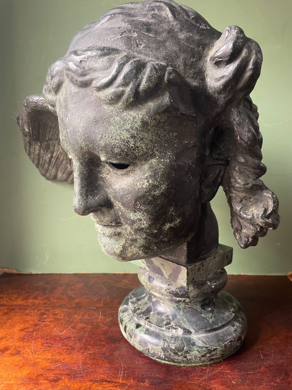 A 19th-century verdigris bronze head study of Hypnos featuring a winged temple, mounted on a round variegated green marble base. View XVI